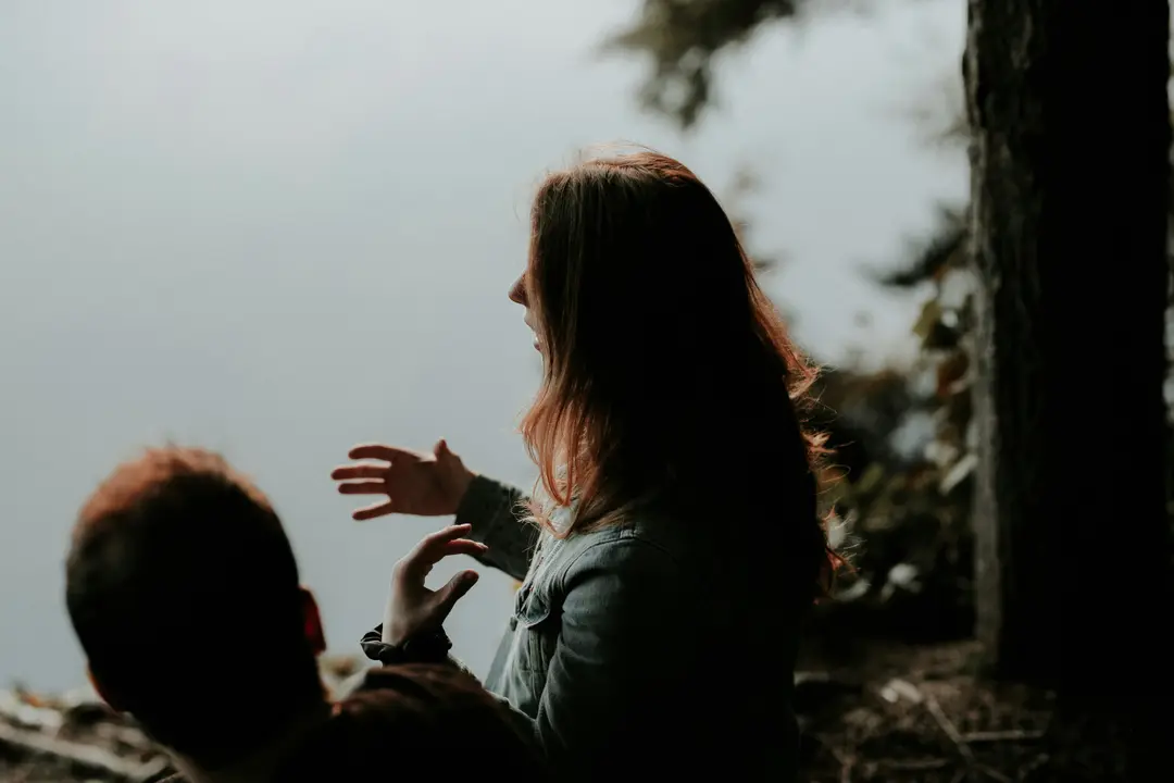 A woman crouching to meet a small child, hands outstretched, among trees